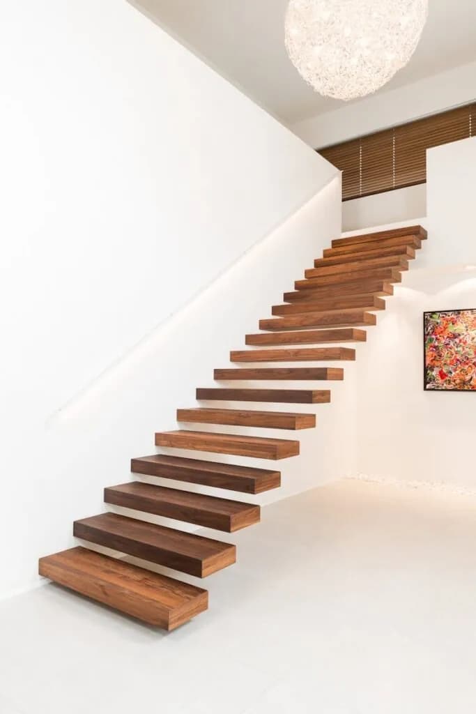 Escalier aux marches épaisses en bois foncé encastrées dans un mur blanc, vu de côté, tableau coloré au fond de la pièce