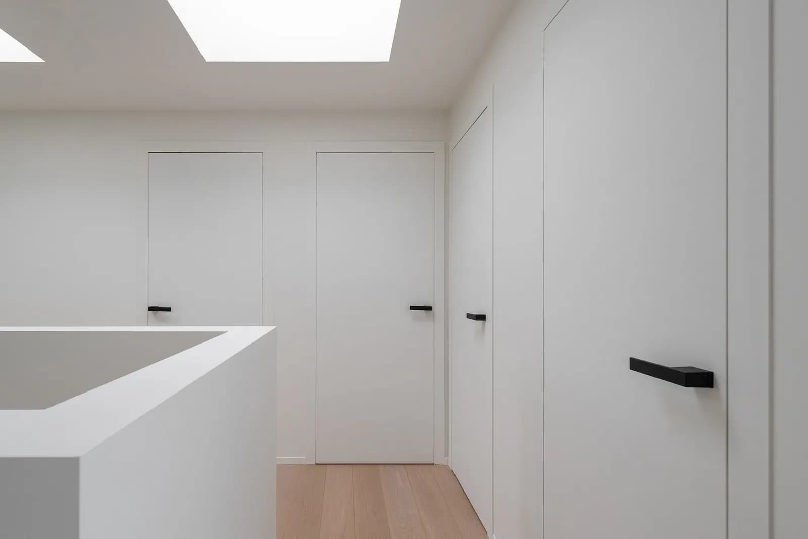 Palier blanc éclairé par un puits de lumière, portes blanches sans encadrement apparent, sol en bois clair